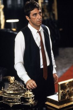 a man wearing a vest and tie standing in front of a table with gold objects