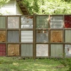 a fence made out of old windows in the grass with trees and bushes behind it