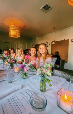 two women sitting at a table with flowers and candles