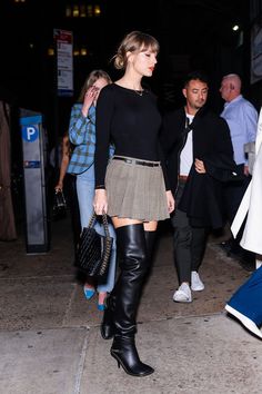 a woman is walking down the street wearing black boots and a skirt with high heels