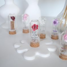 small bottles with flowers in them sitting on a white counter top next to vases