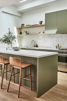 two wooden stools sit in front of an island counter with white countertops and green cabinets