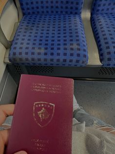 a person holding a red passport in front of two blue seats on a subway train