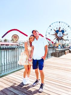 a man and woman standing on a boardwalk next to a ferris wheel at an amusement park