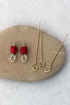 three pairs of red earrings sitting on top of a rock next to some gold wire