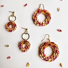 three pairs of earrings on a white surface with pink and yellow petals scattered around them