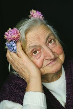 an older woman holding flowers in her hand and looking at the camera with surprise on her face