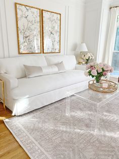 a living room with white furniture and flowers in vases on the coffee table next to the couch