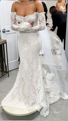 a woman in a white wedding dress standing next to a mirror with her arms crossed