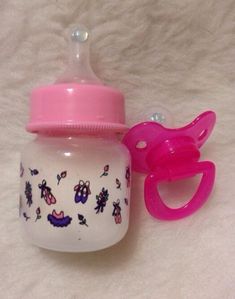 a baby bottle with a pink handle next to a pair of scissors on a white blanket