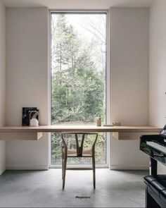 an empty room with a desk and piano in front of a large window that looks out onto the woods