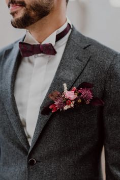 a man wearing a gray suit with a red bow tie and flower boutonniere