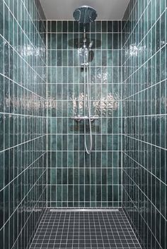 a walk in shower sitting next to a green tiled wall and floor covered in glass tiles