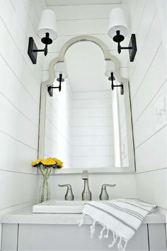 a white sink sitting under a large mirror next to a light fixture with two lights on it