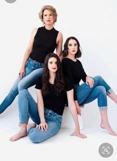 three women are sitting on the floor posing for a photo in jeans and black tops