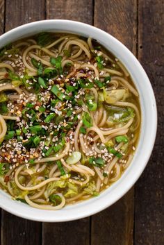 a white bowl filled with noodles and vegetables on top of a wooden table next to chopsticks