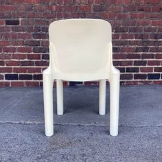 a white plastic chair sitting in front of a brick wall