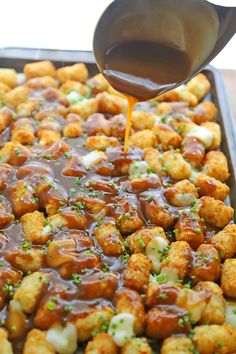 a pan filled with tater tots being drizzled with gravy