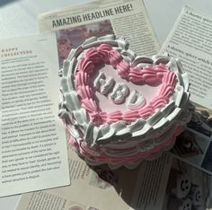 a heart shaped cake sitting on top of a table next to an open book and magazine