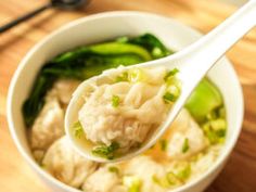 a white bowl filled with dumplings and broccoli on top of a wooden table