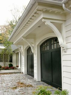 a white house with black garage doors and brick walkway