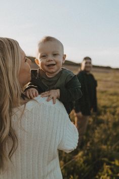 a woman holding a baby in her arms while standing next to two other people on a field