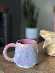 a coffee cup sitting on top of a wooden table next to a potted plant