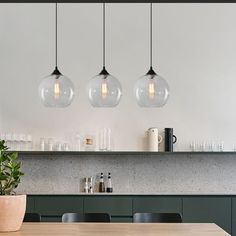 three clear globe lights hang over a kitchen table with black chairs and green cabinetry