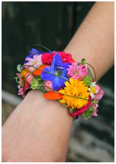 a woman's arm with a colorful flower bracelet on her left wrist and flowers in the middle