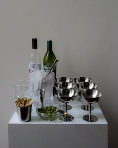 wine glasses, silverware and bottles on a white countertop with food in bowls