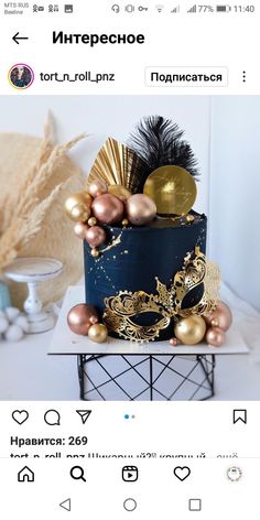 a blue cake with gold decorations and feathers on top, sitting on a table in front of a white wall