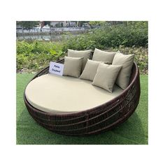 an outdoor wicker day bed with pillows on the grass in front of some bushes