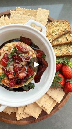 a white bowl filled with food next to crackers and strawberries