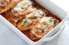 a white casserole dish filled with meat and cheese covered in sauces on a marble counter top