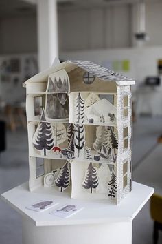 a paper model of a house with trees on the front and sides, sitting on top of a white pedestal