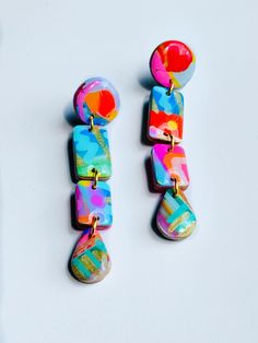 two pairs of colorful earrings on a white surface, one is dangling from the other