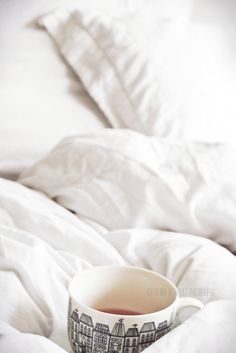 a cup of tea sitting on top of a bed covered in white sheets and pillows