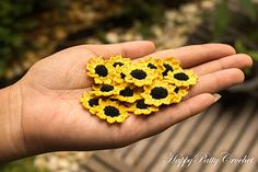 a person's hand holding small yellow and black crocheted sunflowers