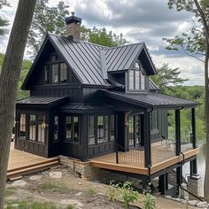 a large black house sitting on top of a wooden deck next to a forest filled with trees