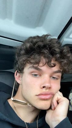 a young man with curly hair sitting in the back seat of a car looking at the camera