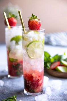 two glasses filled with ice and strawberries on top of a table next to green leaves