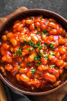 a wooden bowl filled with baked beans and garnished with parsley on top