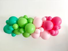 several balloons are arranged in a row on a white surface, one is green and the other is pink