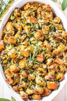 a casserole dish filled with stuffing and topped with fresh rosemary sprigs