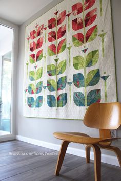 a wooden chair sitting in front of a wall hanging quilt