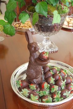 chocolate bunny sitting on top of strawberries in front of a glass bowl filled with flowers