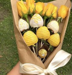 a bouquet of yellow roses wrapped in brown paper with chocolate candies on top and white ribbon