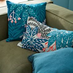 three pillows are sitting on a couch in front of a window with blue and green accents