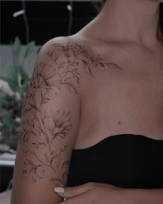 a woman wearing a black strapless top with flowers on her arm and shoulder tattoo