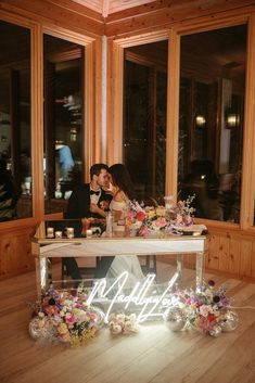 a bride and groom sitting at a table with flowers on it